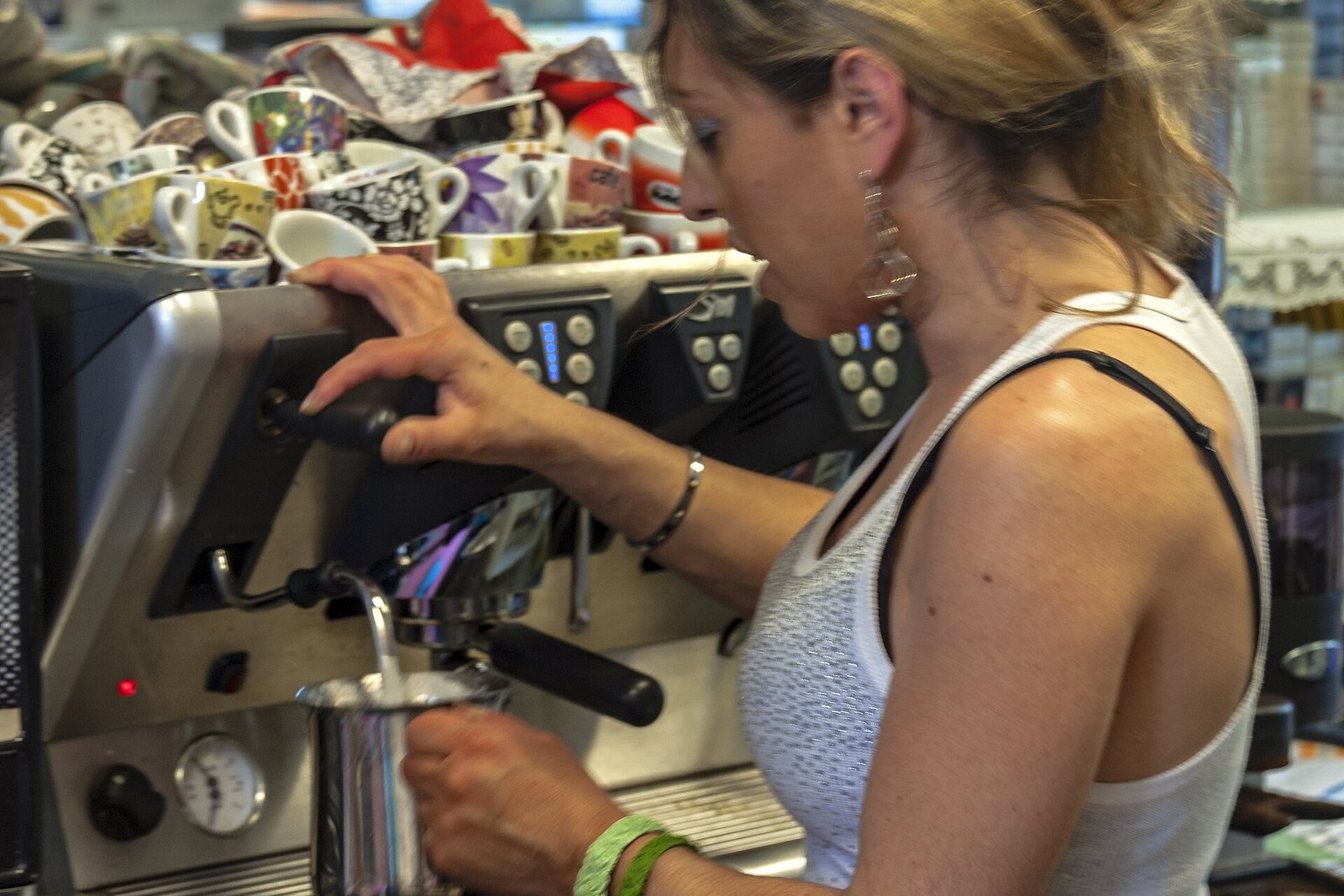 Barista frothing milk in a stainless-steel pitcher beside an espresso machine
