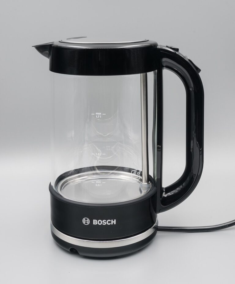 Clear glass electric kettle with a black handle on a neutral background